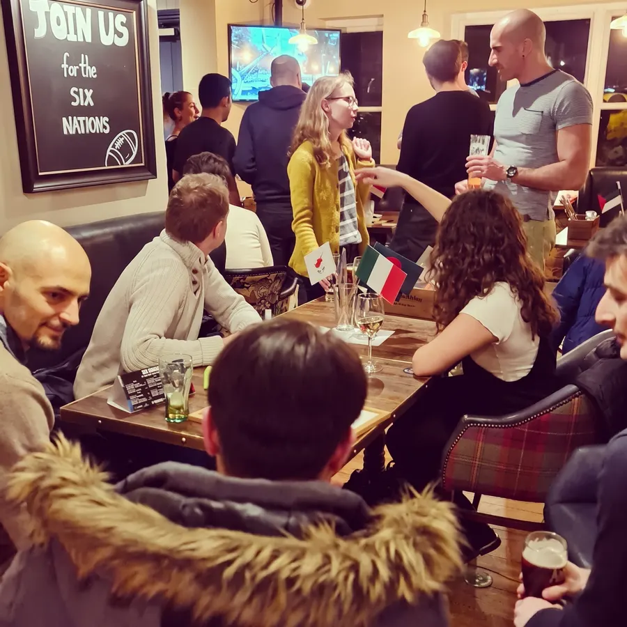People chatting across tables with flags at a busy Guildford Babel evening